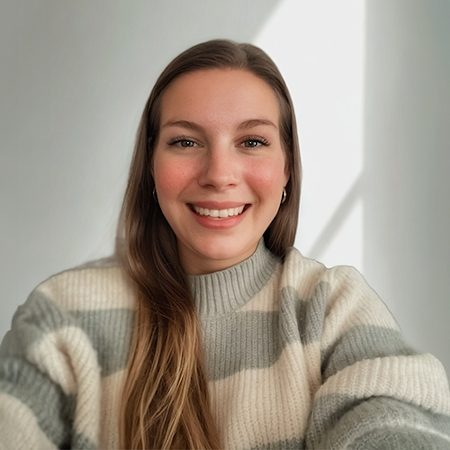 Das Bild zeigt eine Person in einem hellen Raum, die einen gestreiften Pullover trägt. Der Pullover hat breite horizontale Streifen in Grau und Weiß. Der Hintergrund ist neutral gehalten, möglicherweise eine weiße Wand, durch die Licht eines Fensters scheint.