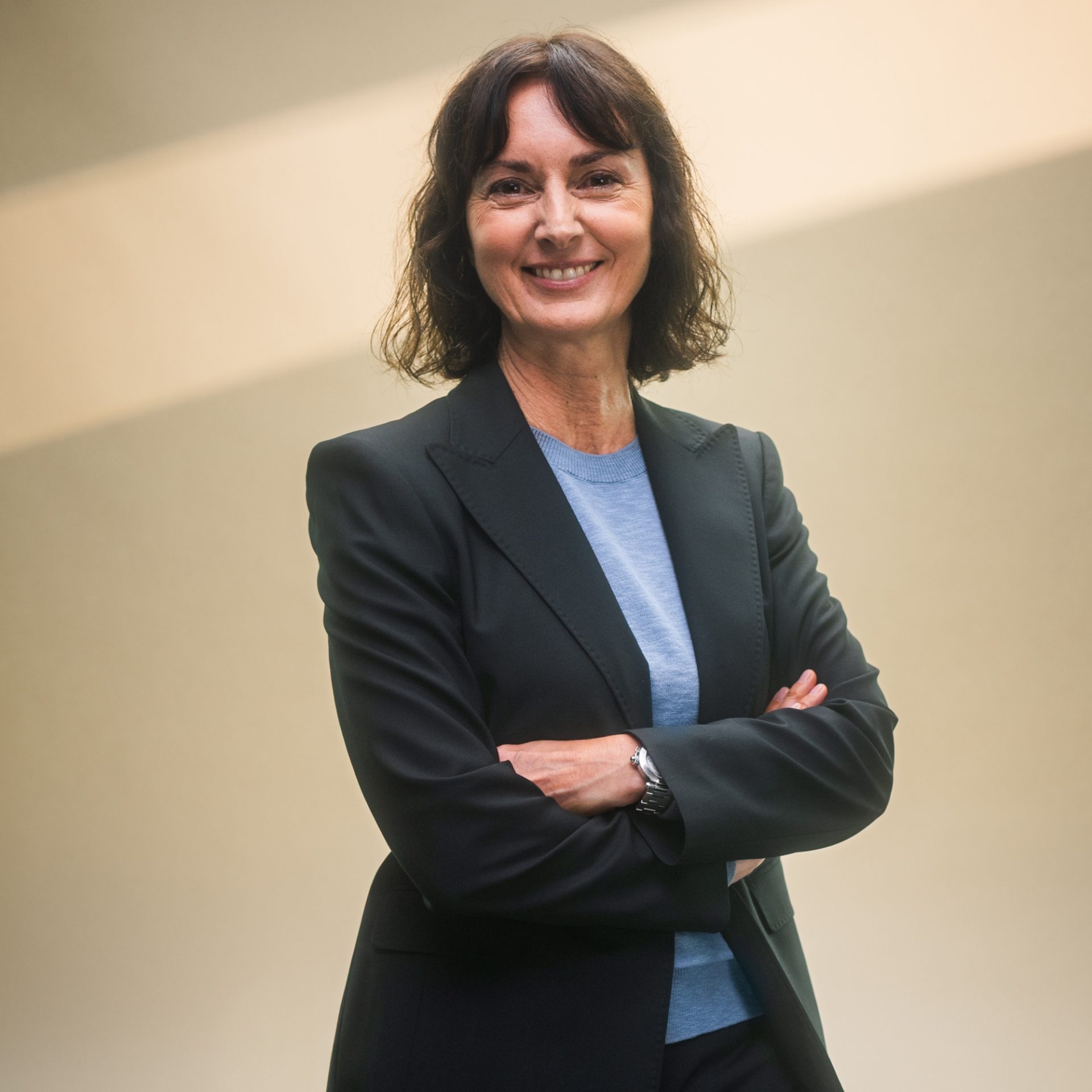 Eine Person in einem dunklen Anzug steht mit verschränkten Armen.