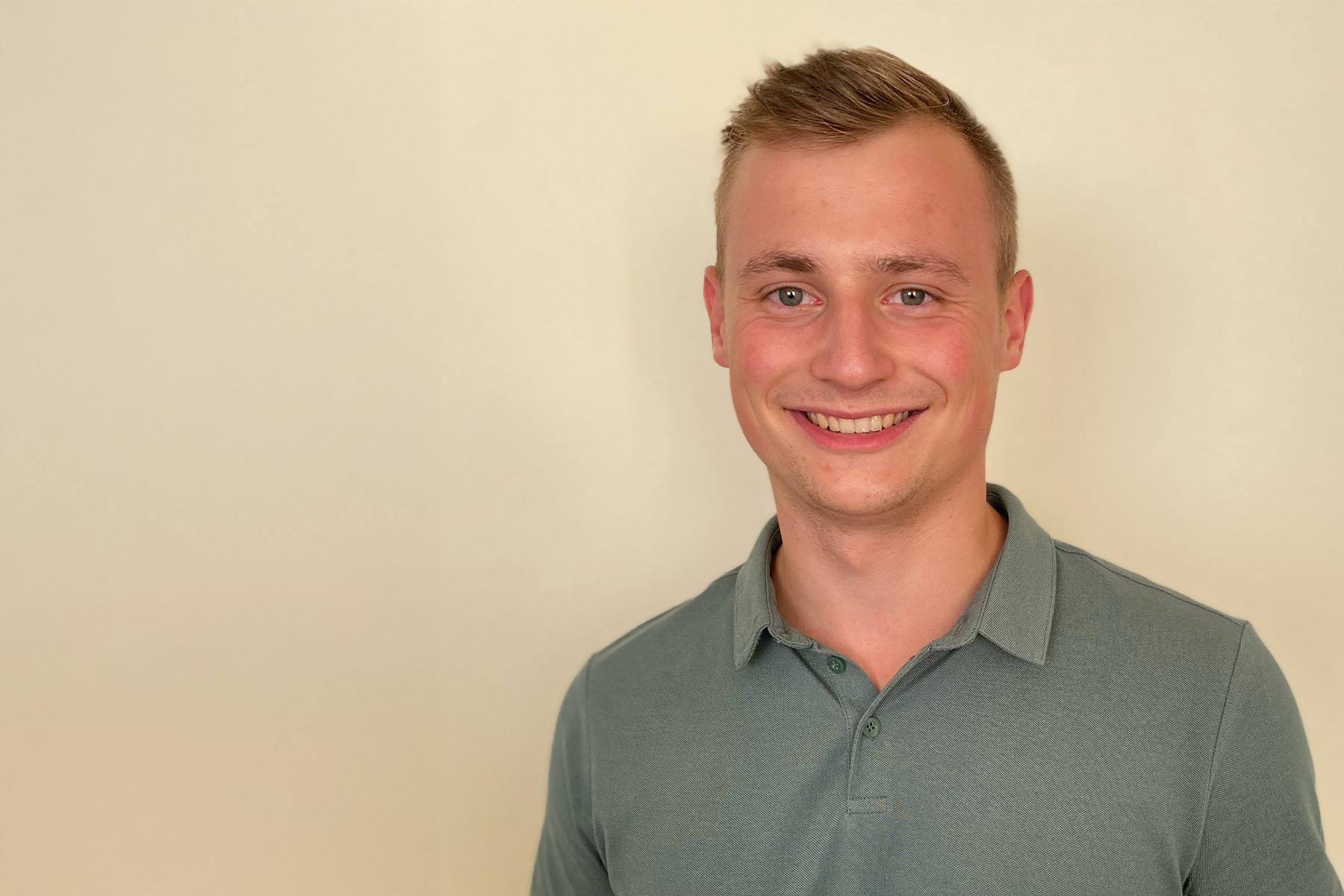 Die abgebildete Person trägt ein hellblaues Poloshirt mit einem Kragen. Der Hintergrund ist einfarbig hellcremefarben.