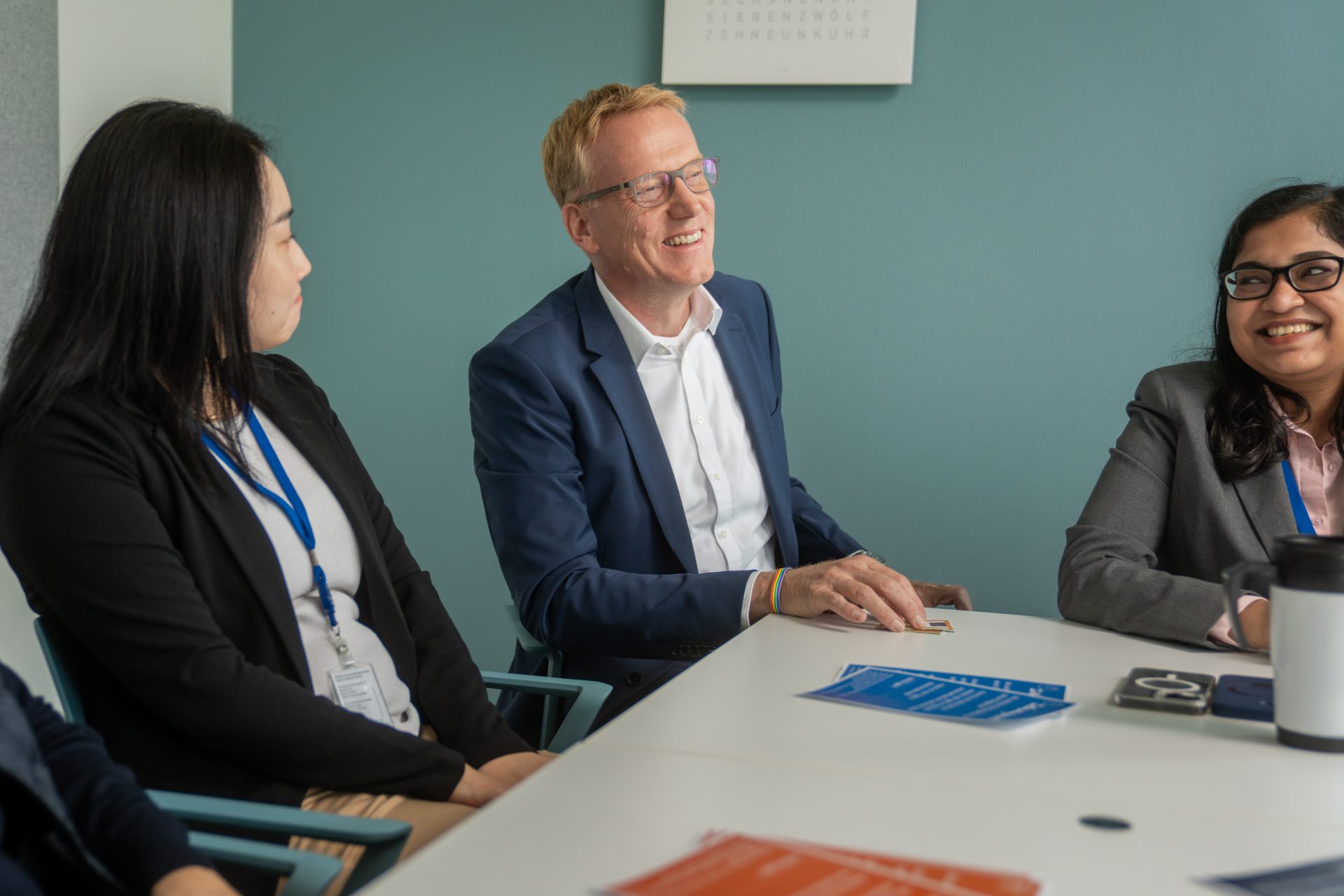 Ein Meeting oder eine formelle Besprechung, bei der mehrere Personen an einem Tisch sitzen und Dokumente vor sich haben. Die Atmosphäre wirkt professionell und bezieht sich vermutlich auf ein Büro-Setting.