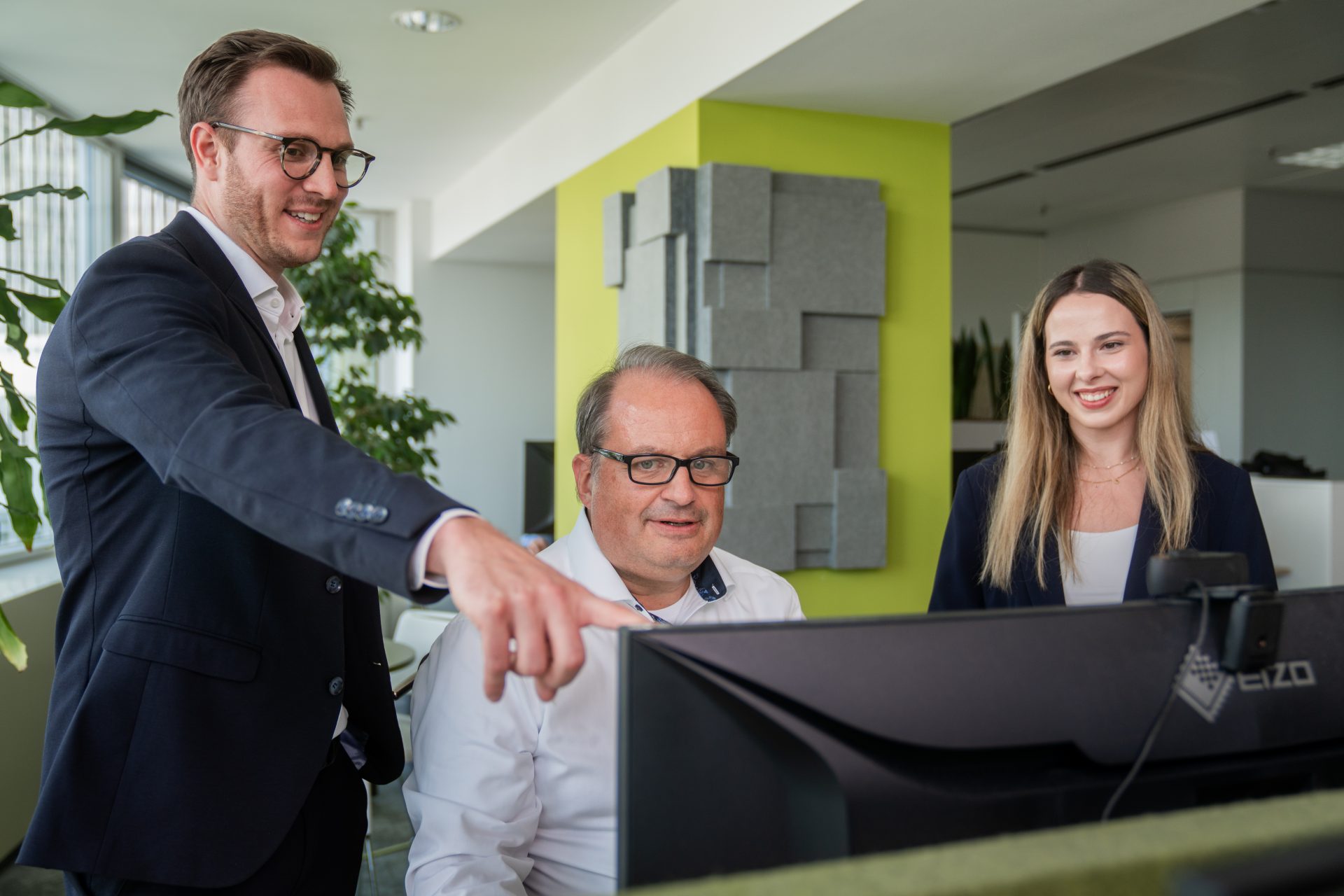 Ein Büro mit einem Computerbildschirm, Pflanze und Wanddekoration.