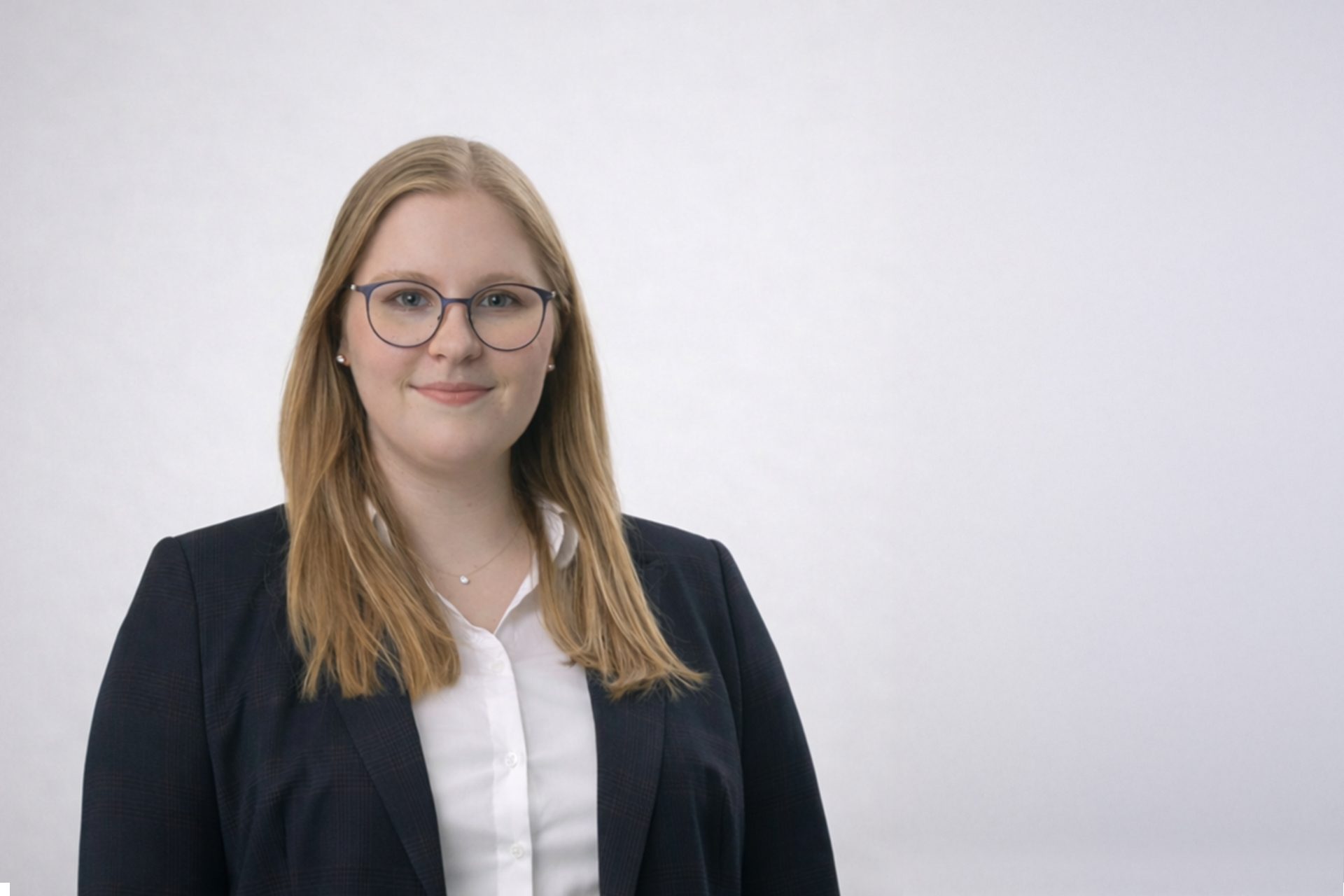 Das Bild zeigt eine Person in formeller Kleidung, bestehend aus einem dunkelblauen Blazer und einem weißen Hemd. Der Hintergrund ist hell und neutral.